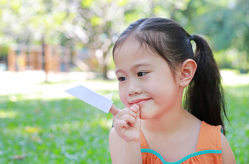 Portrait of little child girl showing a white paper rocket on her forefinger at the nature park. Education and imagination concept.