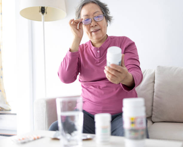 Femme âgée lisant le contenu d’une boîte de médicaments à la maison - Photo