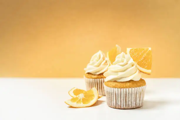 Vanilla cupcakes decorated with orange slices and topped with butter cream frosting - front view on yellow background