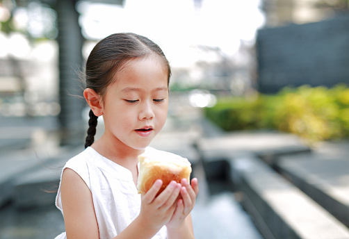 Portrait of Asian little girl eating bread with Stuffed Strawberry-filled dessert in garden outdoor.