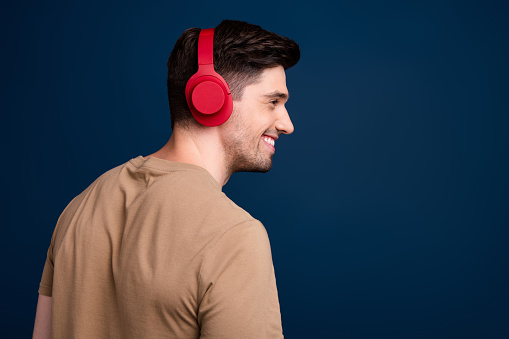 Side profile photo of positive man dressed beige t-shirt in headphones look at promo empty space isolated on dark blue color background.