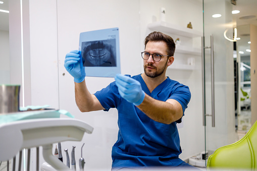 The dentist carefully studies the X-ray with a focused expression, ensuring thorough examination and diagnosis for the patient's dental health.