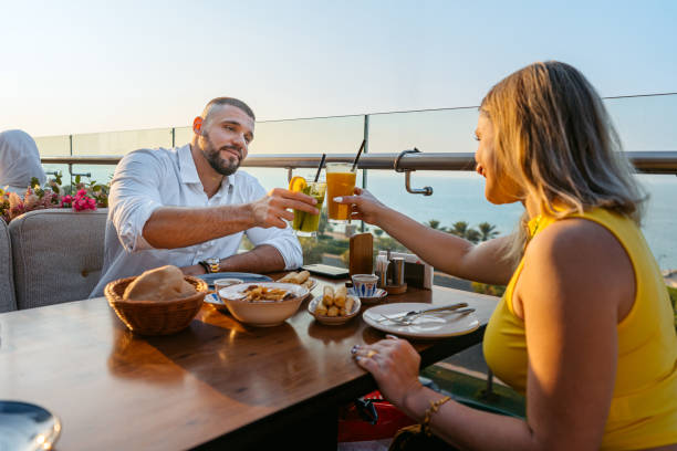 Young Couple Cheering With Drinks While Having Lunch In A Restaurant In Kuwait City