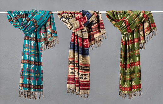 An assortment of colorful woolen blankets, stoles, scarves with fringes. Studio shot, close-up.