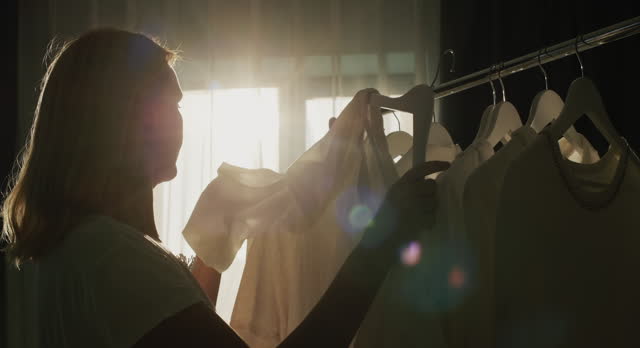 A woman chooses clothes in the dressing room. Silhouette in the sun, side view