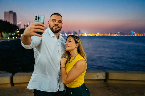 Young couple taking selfies using a smart phone in Kuwait City In Kuwait at night