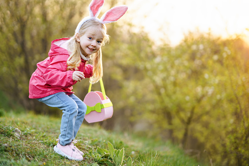 cute blond little girl with rabbit ears and casual outfit holding Easter egg in hand. Easter concept, Easter hunting