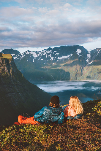 Couple in sleeping bags on a bivouac in Norway mountains with camping travel gear. Friends hiking, enjoying romantic vacations active healthy outdoor lifestyle together