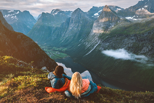 Romantic couple in sleeping bags enjoying bivouac in Norway mountains, friends man and woman hiking with camping travel gear, Valentines day outdoor vacations active healthy lifestyle adventurous trip