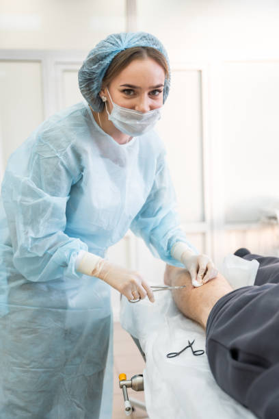 istock Smiling dermatologist surgeon stitching up a wound after skin surgery, close up view of operation process 2007449995
