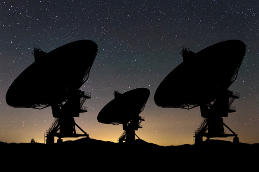 Silhouettes of three large radio telescopes against a starry night sky, capturing the grandeur of space exploration