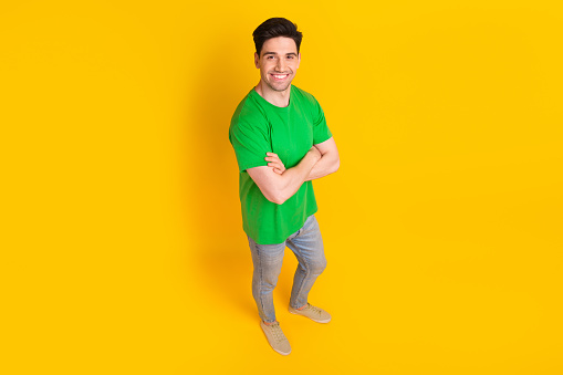 Full size photo of positive cheeful optimistic guy wear stylish t-shirt standing hold hands crossed isolated on yellow color background.
