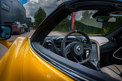 View from the driver's side into a yellow McLaren 765LT's luxurious interior, featuring a leatherwrapped steering wheel with beige stitching, and a hightech console.