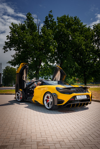A vibrant yellow McLaren 765LT with open dihedral doors, showcasing its aerodynamic shape and luxurious interior, parked outdoors under a clear blue sky.