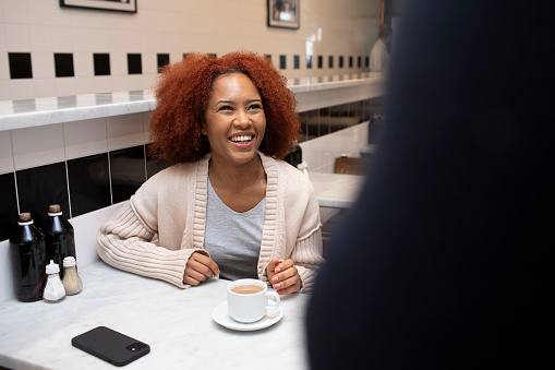Part of a series - Two cheerful female friends are meeting for a coffee and a chat in a traditional-looking British cafe.