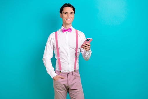 Photo portrait of handsome young guy hold device comment post dressed stylish pink garment isolated on aquamarine color background.