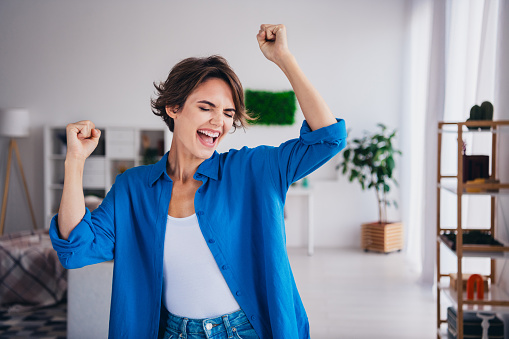 Portrait of delighted overjoyed person raise fists shout yes hooray accomplishment spacious flat indoors.