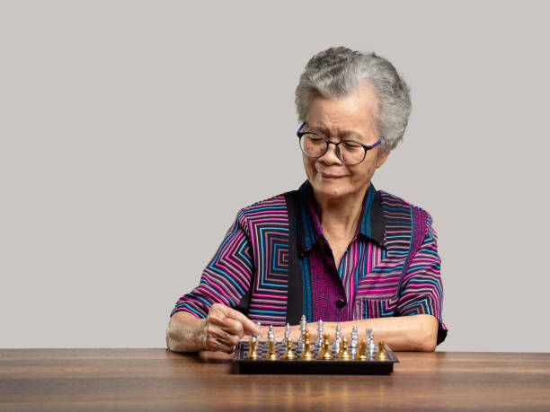 senior woman playing a game of chess on a chessboard while sitting at the table - chess board room business strategy photos et images de collection