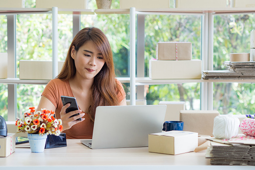 Business woman wear casual cloth sitting working at her office. Work desk for entrepreneur in the office have boxes package, a coffee cup, flower vase and parcel prepare for orders from customers