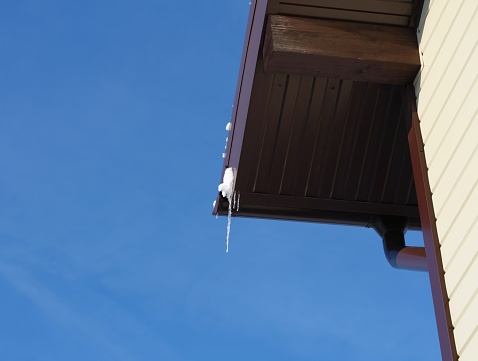 An edge of the roof with a little bit snow and icicles against the blue sky