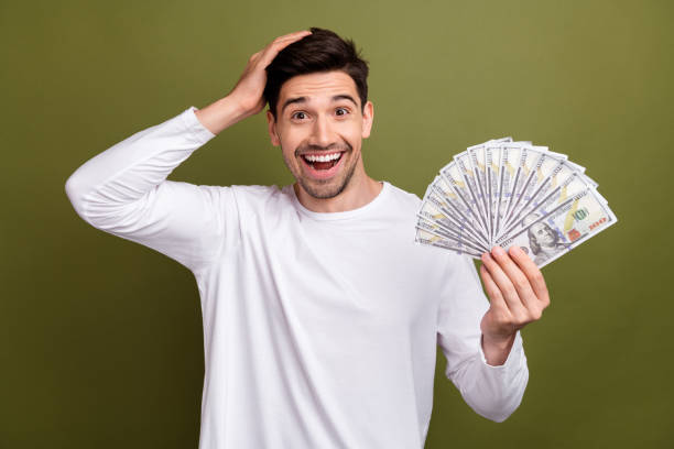 istock Photo of young business man in white pullover holding banknotes when realizes that he has become rich isolated on khaki color background 2007538558