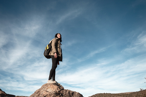 young latin caucasian woman, tourist standing on a stone contemplating the landscape in the mountains of cordoba argentina, with the sky in the background and copy space.