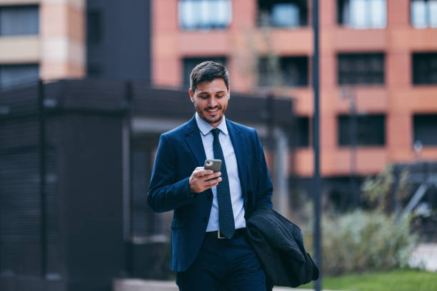 istock Handsome Smiling Man in a Suit on His Way To Work Texting on His Mobile Phone 2007576222