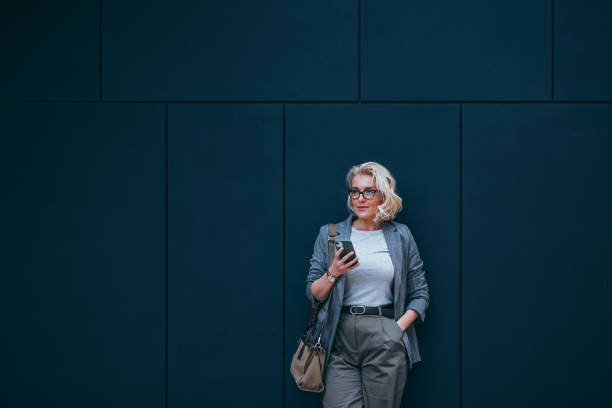 istock Beautiful Businesswoman Leaning Against a Wall While Waiting for Someone and Using Mobile Phone 2007576246