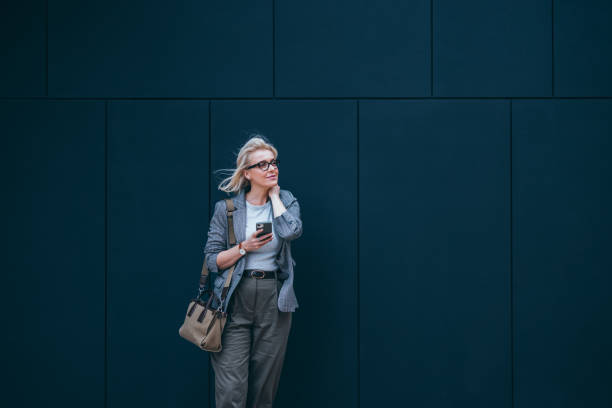 istock Beautiful Businesswoman Leaning Against a Wall While Waiting for Someone and Using Mobile Phone 2007576248