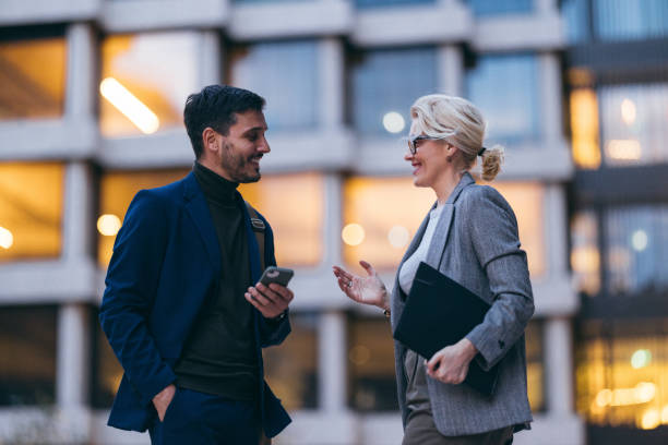 un guapo hombre de negocios y una hermosa mujer de negocios hablando por la noche frente al edificio de oficinas - business two people talking building exterior fotografías e imágenes de stock