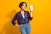 Portrait of confident smart girl wear plaid shirt demonstrate smartphone touch screen empty space isolated on yellow color background