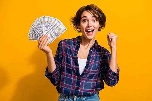 Photo of overjoyed satisfied woman with short hairdo dressed plaid shirt hold money win gambling isolated on yellow color background.
