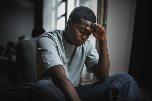 Moment of depression, loneliness and emotional stress. Young black man sits on the floor and looks very upset and stressed