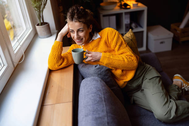 istock Woman relaxing on the sofa while drinking coffee and looking through window 2007594504
