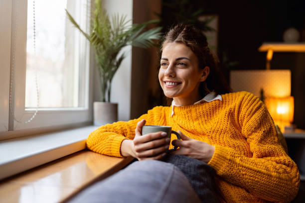 istock Woman relaxing on the sofa while drinking coffee and looking through window 2007594524