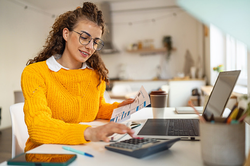 Young Caucasian woman using calculator, while organizing home finances