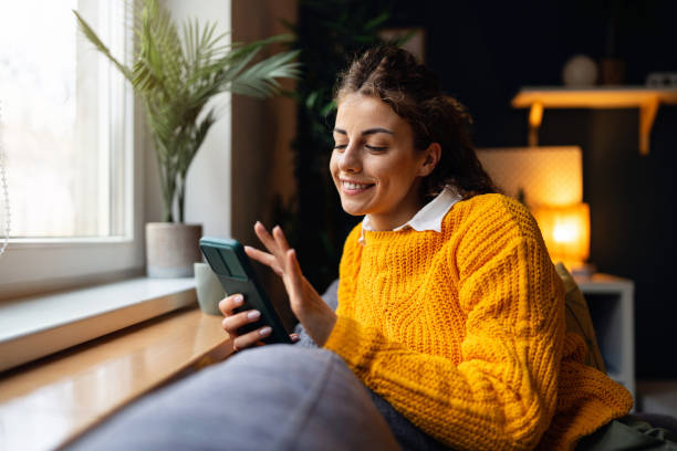 istock Young woman playing video games on mobile phone, while relaxing on the sofa 2007594687