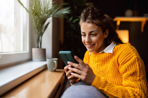 istock Young woman playing video games on mobile phone, while relaxing on the sofa 2007594701