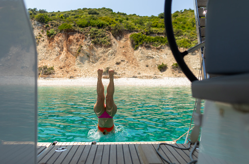 Woman on vacation have a fun while jumping into the sea from sailboat stern