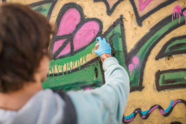 rückansicht eines männlichen straßenkünstlers zeichnet graffiti an die wand eines verlassenen gebäudes, nahaufnahme - graffiti men wall street art stock-fotos und bilder