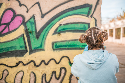 Young female street artist draws graffiti using colorful sprays
