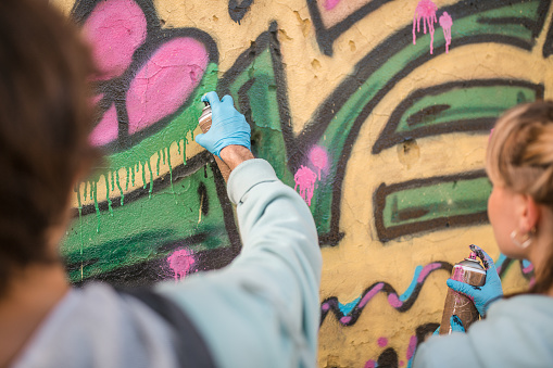 Two young street artist best friends draw colorful graffiti with sprays