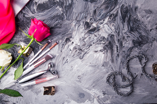 Glamorous makeup tools and fresh flowers set against a monochrome fluid art background.