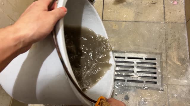 Draining dirty water from a grey bucket into a gutter with dirty tiles