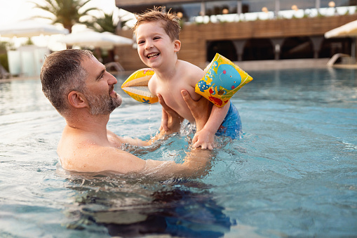 A 6 year old mixed race African-American and Caucasian boy having fun in a swimming pool, laughing and looking at the camera.