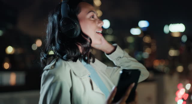 Businesswoman, cellphone and headphone in city at night, scroll and listening to online music playlist on balcony. Journalist, dancing or streaming podcast on mobile app and relax on rooftop in town