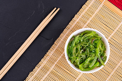 Chuka seaweed salad in a white plate with chinese chopsticks on a mat top view