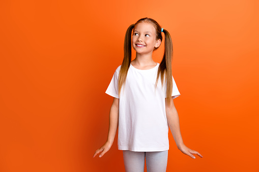 Photo portrait of charming little girl look interested empty space cute pose wear trendy white clothes isolated on orange color background.