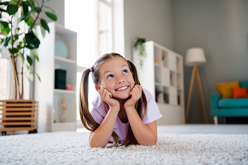 Photo of cheerful creative minded girl lying carpet floor look away fantasize imagine apartment indoors.