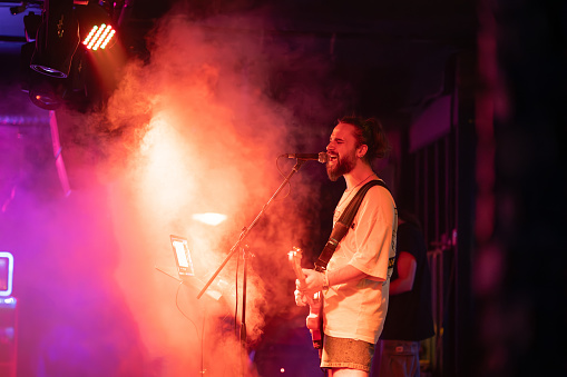 Silhouette of guitar player on stage. Dark background, smoke, spotlights